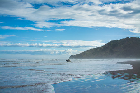A pair of surfers walking into breaker water at Makorori Beach, mist rising over water obscuring distant mountains. Gisborne, New Zealandの写真素材