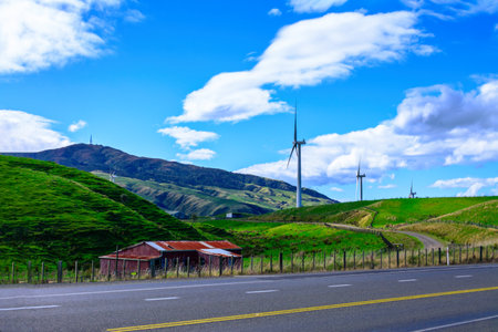 Breathtaking landscape of lush green hills and wind farm against blue sky and white clouds. Concept of alternative energy and sustainability. Palmerston North, New Zealand.の写真素材