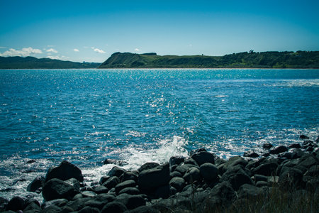 Rocky beach on a bright sunny day. Rocky shoreline with turquoise water and cloudless sky. Many Bay, looking towards estuary of Tawatahi River. Raglan, New Zealandの写真素材
