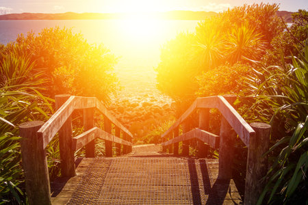 Coastal path with wooden steps down to the rocky coastline. Bright light beckoning and promising hopeの写真素材