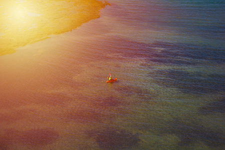 A lone kayaker paddles through calm, shallow waters under the warm golden glow of the sun. The...