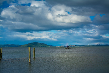 A pair of seaplanes rest on the calm waters of Lake Rotorua under dramatic storm clouds, ready for...
