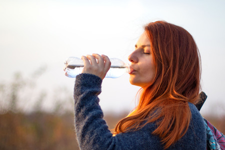 Young redhead girl drinks water  in autumn sunny dayの写真素材