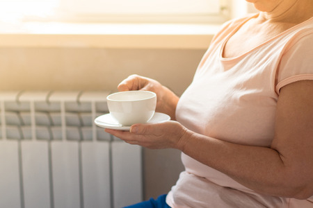 Mid adult woman drinking coffee and looking out of the window on sunny day. Horizontal shapeの写真素材