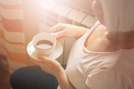 Enjoying coffee time at home. Woman and coffee in hands looking through the glass windowの写真素材