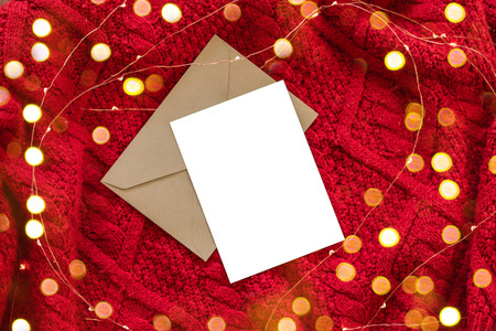 Christmas composition of mockup card with lights on red knitted background. Flat lay, top view, copy space, square.の写真素材
