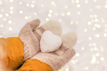 Hands in warm knit mittens with a snowy heart on a background of snow, Valentine's Day romantic conceptの写真素材