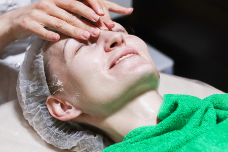 Woman getting facial care by beautician at spa salon, side view, close-up.  Face skin care.の写真素材