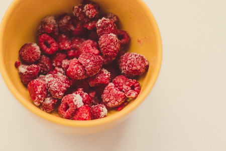 Close-up bright juicy raspberry berries in a yellow bowl on a white backgroundの写真素材