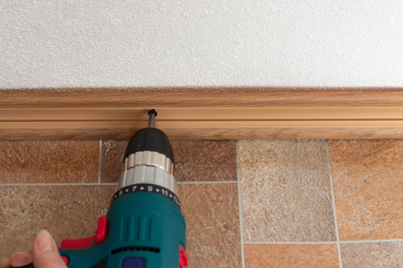 Worker with a screwdriver in his hands mounts a floor plinthの写真素材