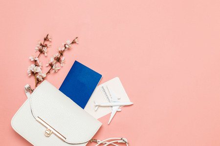 Tourist travel concept. Women's white bag with international passport, ticket and a sprig of flowers on living coral backgroundの写真素材