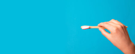 Female hand holding bamboo natural brush with toothpaste on blue background