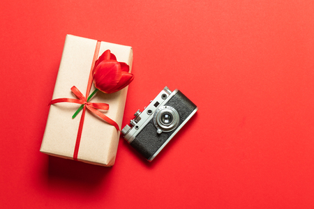Surprise gift box with a red ribbon and a tulip on a red background, an old model photo cameraの写真素材
