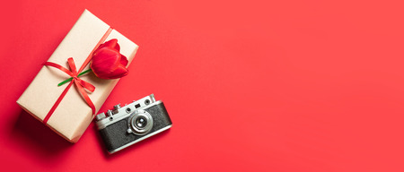 Red tulips, gift box and camera on red background. Flat lay, top view, copy spaceの写真素材