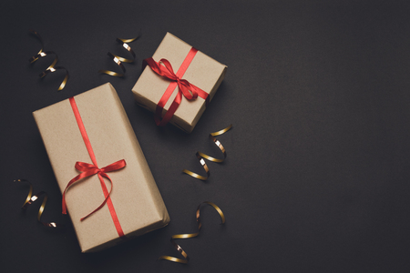Gift box wrapped in craft paper with red ribbon and gold decor on black stone. Birthday party backgroundの写真素材