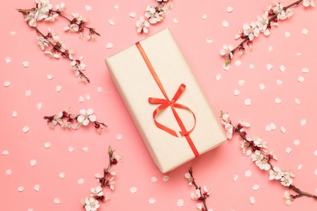 Gift surprise box with sprigs of flowers and petals on a pink backgroundの写真素材