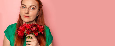 Smiling girl in a green bright dress with a pink bouquet of tulips on a pink background