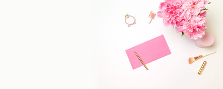 Top view of a pink paper envelope with a gold pen, womens accessories, a bouquet of pink peonies,...