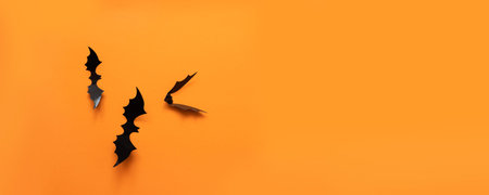 Creative top view flat lay autumn halloween composition of black paper bats fly up on an orange...