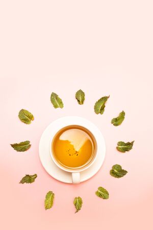 Creative spring concept of white ceramic cup with herbal green or black tea with mint leaves on a pink background. Flat lay, top view.の写真素材