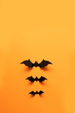 Creative top view flat lay autumn halloween composition of black paper bats fly up on an orange backgroundの写真素材