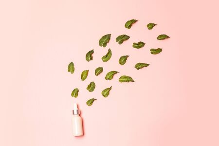 Natural anti-aging serum liquid dropper in a glass tube with mint petals on a pink background. Flat lay, top view.の写真素材