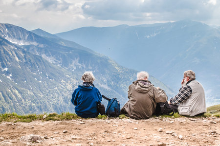 Polish Tatras, Poland June 3 2019: Three elderly people with backpacks are sitting on in the...