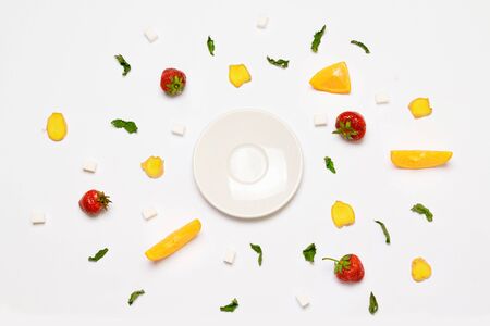 Flat lay concept empty white plate, sugar cubes, strawberries, ginger slices, orange and mint leaves. Objects are arranged in the form of a circle.の写真素材