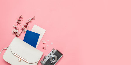 Top view of traveler outfit on pink background with copy space, flat lay summer and travel concept. White bag, photo camera, flowers and passportの写真素材