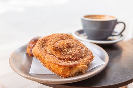 Warm cinnamon bun with icing sugar with a cup of coffee lying in a street cafe.の写真素材