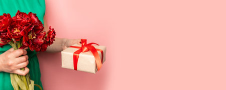 Concept of holidays and surprises. Female hands hold a box with a gift in a bouquet of red tulips