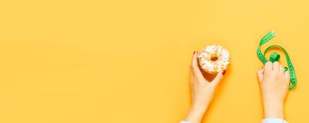 Female hand holding sweet biscuit and measuring tape over orange background. Concept of diet and healthy eatingの写真素材