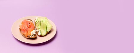 Food and proper nutrition concept. Tasty fresh sandwich with red fish, feta cheese cucumber and pesto on a pink ceramic plate on a purple backgroundの写真素材