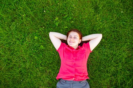 Portrait of a smiling red-haired young girl on green grass. Rest and relaxation concept.の写真素材
