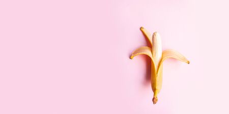 Juicy summer vitamin concept. Flat composition of sweet opened banana on pink background with copy space for your text.の写真素材