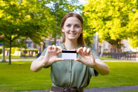 Mockup online shopping concept. Blonde girl in a summer green dress with a plastic card in a park outdoors.の写真素材