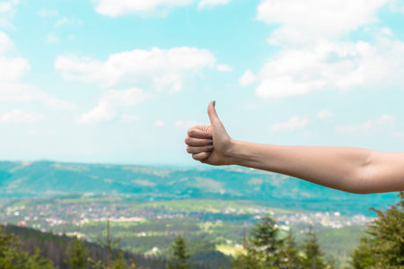 Hand shows thumbs up on the background of mountains