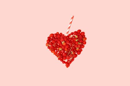 Assorted ripe red berries of raspberries, currants and strawberries with a striped cocktail straw on a pink background. Summer food conceptの写真素材