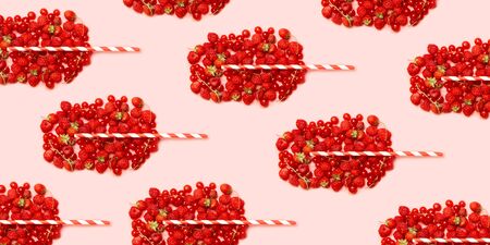 Summer fruit concept pattern. Different red ripe berries in the shape of a glass with fruit juice and a straw on a pink backgroundの写真素材
