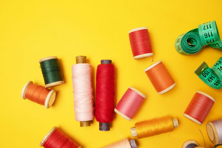 Sewing accessories and fabric on a yellow background. Sewing threads, needles, fabric, buttons and...