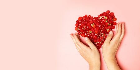 Female hands and red berries in the shape of a heart on a pink background. Health diet heart abstract conceptの写真素材