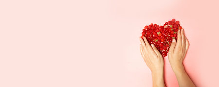 Female hands and red berries in the shape of a heart on a pink background. Love and recognition...