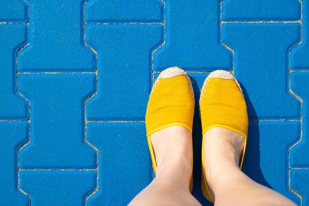 Female legs in yellow shoes or moccasins on a blue tile on a sunny day, summerの写真素材