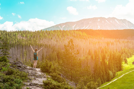 Woman tourist with hands in the air standing on a cliff of rock. Lifestyle travel adventure outdoor...