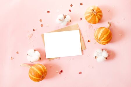 Mockup postcard with craft paper envelope and small pumpkins, glitter decor and cotton flowers on pink background. Minimal style composition, flat lay, view.の写真素材