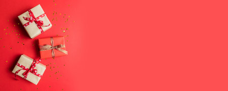 Christmas composition. Gifts or present boxes and stars confetti on red table top view. Creative...