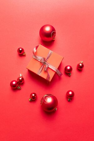 Christmas composition with red present box, ribbons, red big and small balls, holiday decorations on background. Flat lay, top view, copy spaceの写真素材