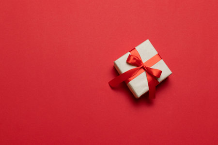 Gift or present box with red ribbon bow on red table top view. Trendy composition for birthday,...