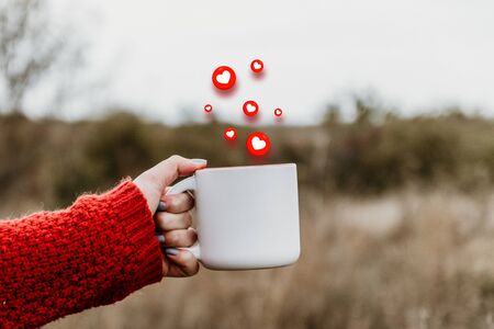 Autumn mood of love. Female hand holds a ceramic cup with soaring in the air love shape emojiの写真素材