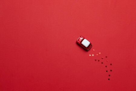 Top view small glossy toy car with golden star sparkles on a red background. Holiday greeting card or banner.の写真素材